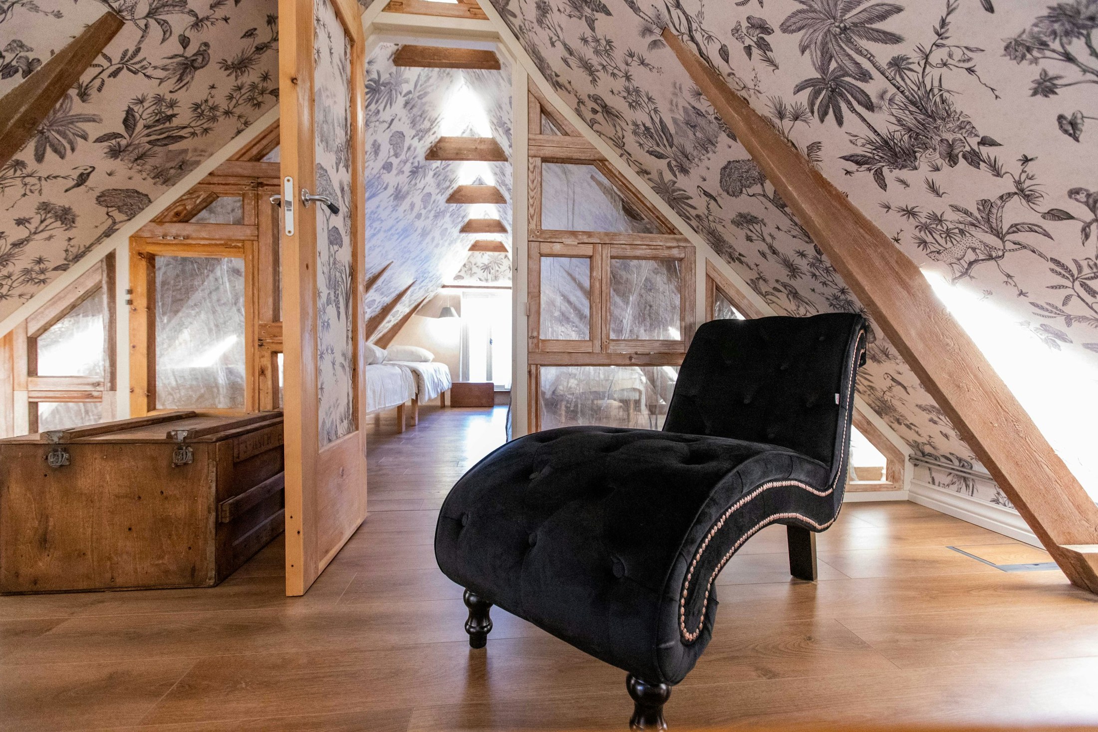 Toile wallpaper following the sloped walls of a timber-framed attic room